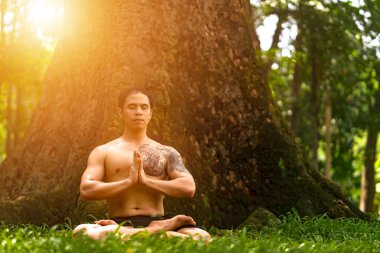 Genç Asyalı adam terini siliyor ve parkta yoga egzersizleri yapıyor. Yoga ve zen kavramı.
