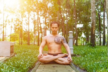 Genç Asyalı adam terini siliyor ve parkta yoga egzersizleri yapıyor. Yoga konsepti.
