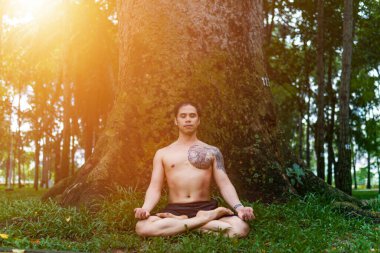 Genç Asyalı adam terini siliyor ve parkta yoga egzersizleri yapıyor. Yoga ve zen kavramı.