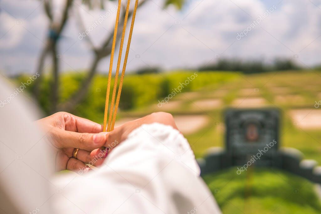close-up of a woman hand holding incense. The background is an unspecified, faded tomb. Concept of spiritual and religious