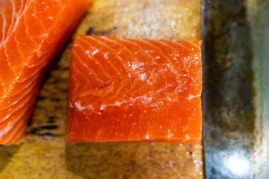 Taze çiğ somon balığı bıçakla kesiliyor ve kesme tahtasının üzerinde yatıyor. Japon somon balığı sashimi. Seçici odak.