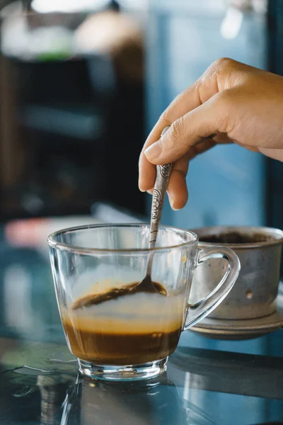 close-up hands of a woman stirring coffee, Hot milk coffee dripping in Vietnam style. Selective Focus. Drink and travel concept