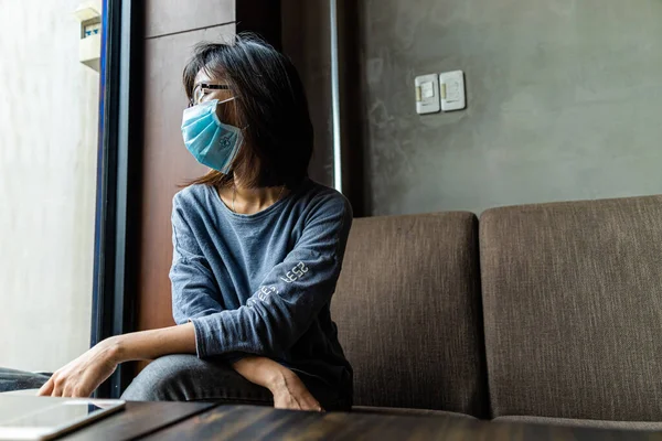 隔離自己隔離 ソファに腰掛けて窓から外を眺める医療マスク姿の若いアジア人女性の悲しみ 社会的距離と医療の概念 — ストック写真