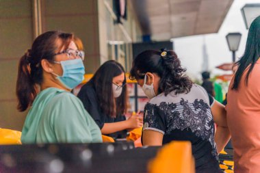 Ho Chi Minh şehri, Vietnam - 08 Ağustos 2020: Yerel halk Emart süpermarketinden alışveriş yapıyor, tıbbi maskeler takıyor, yağmurda motosiklet sürüyor ve Covid-19 salgınında sosyal mesafeyi koruyorlar.