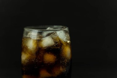 Buzlu, köpüklü ve köpüklü soğuk bir bardak kola. Kola bardakta, buz küpleri koyu arka planda. İçki ve ürün konsepti.