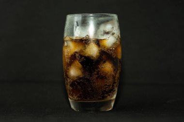 Buzlu, köpüklü ve köpüklü soğuk bir bardak kola. Kola bardakta, buz küpleri koyu arka planda. İçki ve ürün konsepti.