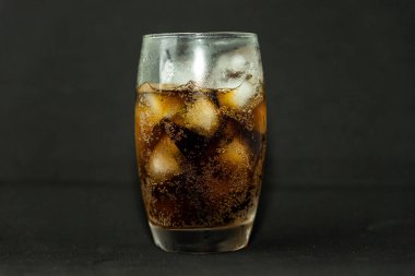 Buzlu, köpüklü ve köpüklü soğuk bir bardak kola. Kola bardakta, buz küpleri koyu arka planda. İçki ve ürün konsepti.