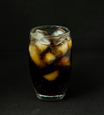 Buzlu, köpüklü ve köpüklü soğuk bir bardak kola. Kola bardakta, buz küpleri koyu arka planda. İçki ve ürün konsepti.