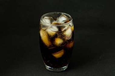Buzlu, köpüklü ve köpüklü soğuk bir bardak kola. Kola bardakta, buz küpleri koyu arka planda. İçki ve ürün konsepti.