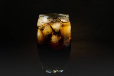 Buzlu, köpüklü ve köpüklü soğuk bir bardak kola. Kola bardakta, buz küpleri koyu arka planda. İçki ve ürün konsepti.