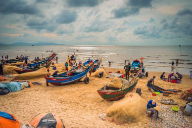 Vung Tau, Vietnam - 22 Ağustos 2020: Geleneksel olarak mavi ahşap tekneleri denizden kıyıya iten yerel balıkçıların manzarası, ağlardan balık avlama sahnesiyle şafak sökerken balıkları toplarlar..