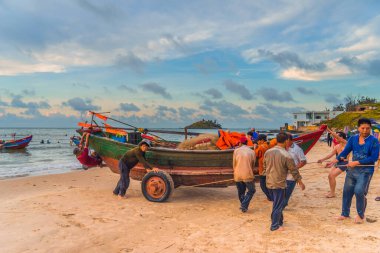 Vung Tau, Vietnam - 22 Ağustos 2020: Geleneksel olarak mavi ahşap tekneleri denizden kıyıya iten yerel balıkçıların manzarası, ağlardan balık avlama sahnesiyle şafak sökerken balıkları toplarlar..