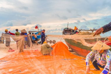 Vung Tau, Vietnam - 22 Ağustos 2020: Geleneksel olarak mavi ahşap tekneleri denizden kıyıya iten yerel balıkçıların manzarası, ağlardan balık avlama sahnesiyle şafak sökerken balıkları toplarlar..