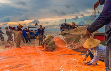 Vung Tau, Vietnam - 22 Ağustos 2020: Geleneksel olarak mavi ahşap tekneleri denizden kıyıya iten yerel balıkçıların manzarası, ağlardan balık avlama sahnesiyle şafak sökerken balıkları toplarlar..