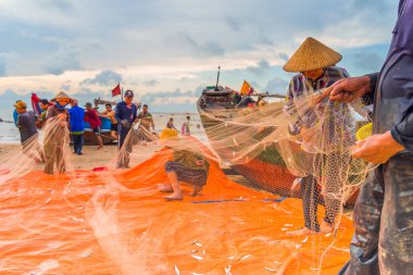 Vung Tau, Vietnam - 22 Ağustos 2020: Geleneksel olarak mavi ahşap tekneleri denizden kıyıya iten yerel balıkçıların manzarası, ağlardan balık avlama sahnesiyle şafak sökerken balıkları toplarlar..