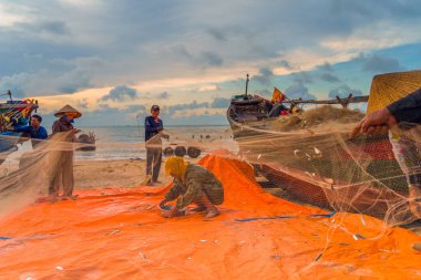 Vung Tau, Vietnam - 22 Ağustos 2020: Geleneksel olarak mavi ahşap tekneleri denizden kıyıya iten yerel balıkçıların manzarası, ağlardan balık avlama sahnesiyle şafak sökerken balıkları toplarlar..
