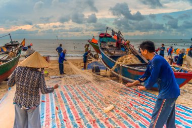 Vung Tau, Vietnam - 22 Ağustos 2020: Geleneksel olarak mavi ahşap tekneleri denizden kıyıya iten yerel balıkçıların manzarası, ağlardan balık avlama sahnesiyle şafak sökerken balıkları toplarlar..