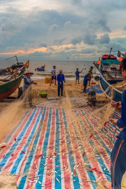 Vung Tau, Vietnam - 22 Ağustos 2020: Geleneksel olarak mavi ahşap tekneleri denizden kıyıya iten yerel balıkçıların manzarası, ağlardan balık avlama sahnesiyle şafak sökerken balıkları toplarlar..
