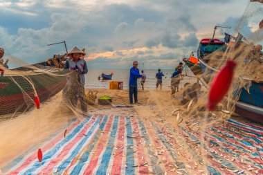 Vung Tau, Vietnam - 22 Ağustos 2020: Geleneksel olarak mavi ahşap tekneleri denizden kıyıya iten yerel balıkçıların manzarası, ağlardan balık avlama sahnesiyle şafak sökerken balıkları toplarlar..