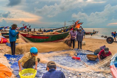 Vung Tau, Vietnam - 22 Ağustos 2020: Geleneksel olarak mavi ahşap tekneleri denizden kıyıya iten yerel balıkçıların manzarası, ağlardan balık avlama sahnesiyle şafak sökerken balıkları toplarlar..