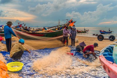 Vung Tau, Vietnam - 22 Ağustos 2020: Geleneksel olarak mavi ahşap tekneleri denizden kıyıya iten yerel balıkçıların manzarası, ağlardan balık avlama sahnesiyle şafak sökerken balıkları toplarlar..