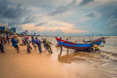 Vung Tau, Vietnam - 22 Ağustos 2020: Geleneksel olarak mavi ahşap tekneleri denizden kıyıya iten yerel balıkçıların manzarası, ağlardan balık avlama sahnesiyle şafak sökerken balıkları toplarlar..