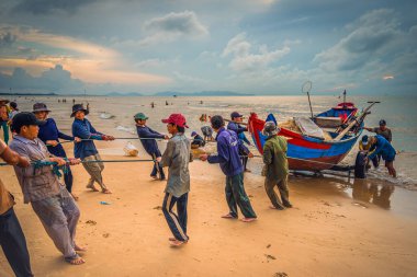 Vung Tau, Vietnam - 22 Ağustos 2020: Geleneksel olarak mavi ahşap tekneleri denizden kıyıya iten yerel balıkçıların manzarası, ağlardan balık avlama sahnesiyle şafak sökerken balıkları toplarlar..