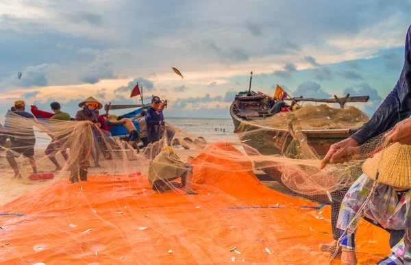 Vung Tau, Vietnam - 22 Ağustos 2020: Geleneksel olarak mavi ahşap tekneleri denizden kıyıya iten yerel balıkçıların manzarası, ağlardan balık avlama sahnesiyle şafak sökerken balıkları toplarlar..