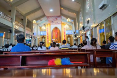 Vietnam 'da, mihrapta, mihrapta büyük bir haçın altında duran papazın, sıralardaki insanlarla dolu bir Vietnam kilisesinin arka planındaki bulanık fotoğraf. Seçici odak.