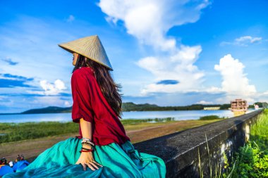 Vietnam 'ın Tay Ninh bölgesindeki Dau Tieng gölünde güzel bir günbatımında mavi gökyüzüyle hendekte oturan Vietnamlı kız. Seyahat ve manzara konsepti.