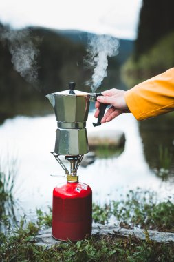 Göl kenarındaki gaz ocağında çay ya da kahve hazırlarken insan eli gayzer kahve makinesini mayalıyor. Kaynar buhar