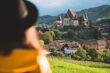 Splendid summer view of Fortified Church of Biertan, UNESCO World Heritage Site.Afternoon cityscape of Biertan town, Transylvania, Romania. Woman wearing a hat in the foreground. Tourist point of view clipart
