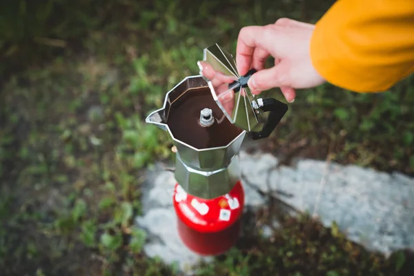 Close up hands of female preparing tea or coffee with italian coffee maker mocca on camping gas stove or cooker. Camping cooking in nature outdoor. Tourism recreation outside and campsite lifestyle.