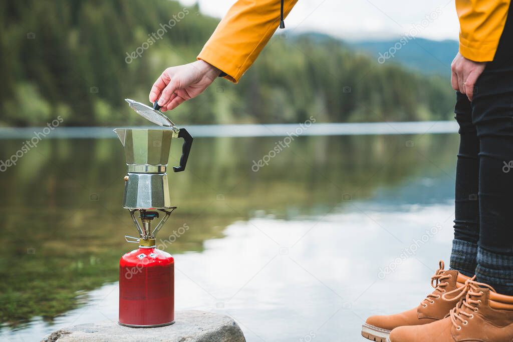 Hands of female preparing tea or coffee with italian coffee maker mocca on camping gas stove or cooker. Camping cooking in nature outdoor. Tourism recreation outside and campsite lifestyle.