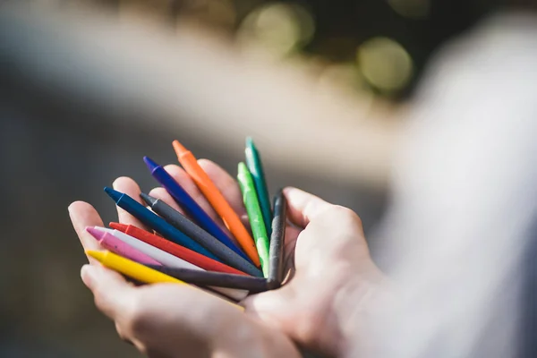 Female hands holding colorful pencils in the park. Bunch of multicolored crayons in hand. Human hand holding color pencils