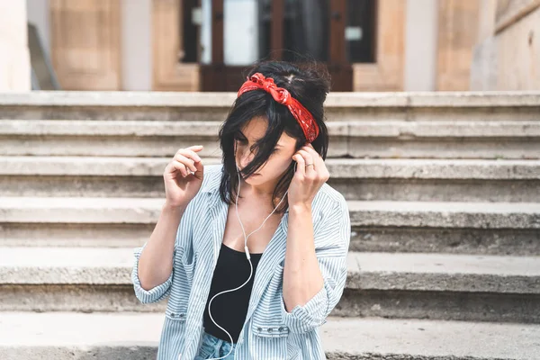 Happy young caucasian woman in striped shirt and earphones, listening to music, while preparing to leave college