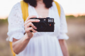 Mladá žena drží retro kameru a fotí. Stylová dáma fotografování s vintage fotoaparátem se západem slunce na pozadí
