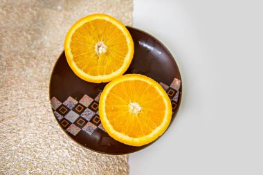 Süslü kahverengi bir tabakta sulu bir portakalın iki yarısı beyaz bir masada altın bir yaprağın arka planında yatar. C vitamini ile Kahvaltı İçin Taze ve Tatlı Tatlı Tatlı.