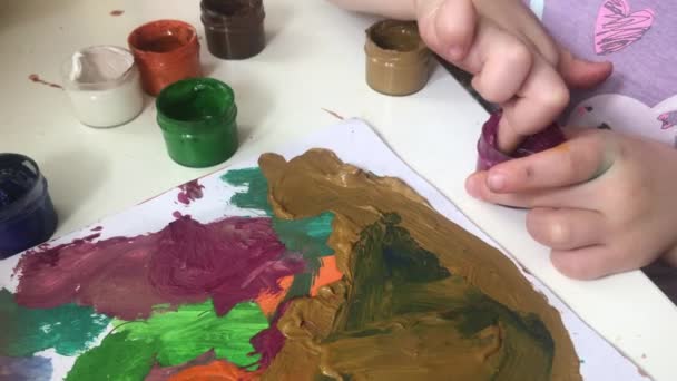 指を持つ少女は筆ではなく指の絵具で紙に描く 家庭での子供の発達に関する授業 就学前の子供の運動技術の開発 選択的焦点 — ストック動画