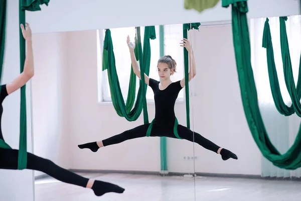 Atletik ve formda bir kız, yeşil hamak tuvali olan beyaz bir odada, spor kıyafetleriyle yoga yapıyor. Sağlıklı yaşam tarzı, esneme, meditasyon ve güzel bir vücut kavramı. Gençler için hobiler