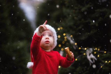 Noel Baba kostümü ve şapkalı güzel bir kızın yakın plan portresi. Noel Baba gökyüzüne bakar ve parmağıyla Noel Baba 'nın geyikli bir kızakla uçtuğunu gösterir. Arka ön odak