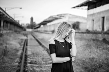 Demiryolunun arka planında dalgın bir sarışın kızın siyah beyaz fotoğrafı. Üzgün, sıkkın, karşılıksız aşk, kırık kalp, genç bir adamdan boşanmak. Acı ve yalnızlık kavramı.