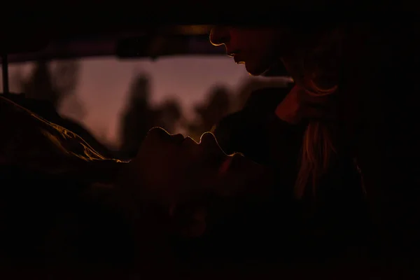 後部座席の車の中で恋人のシルエット 愛情のカップル一緒に夜を過ごすために引退した 女の子は下に横たわっている男にキスをし 彼女の目を調べることにした — ストック写真