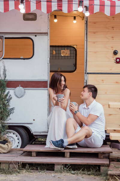 A beautiful couple drinks hot drinks for breakfast early in the morning, talking, looking at each other and laughing. The concept of rest in the country in a caravan. Honeymoon for Just Married