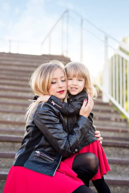 Güzel anne sarışın, kırmızı rujlu ve küçük bir kızı var. Büyük bir portre, kameraya bakıyor, sarılıyor ve gülüyor. Annelik teması ve çocuklu annelerin eğlencesi. Aile görünüşü