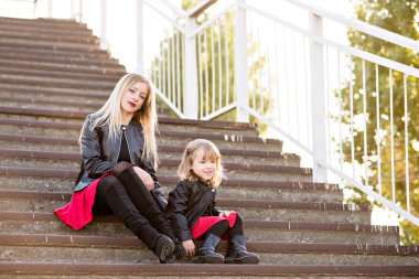 Kırmızı rujlu güzel anne sarışın ve küçük kızı birlikte vakit geçiriyorlar, yürüyorlar, oturuyorlar merdivenlerde koşuyorlar. Kameraya bakıyorlar, sarılıyorlar ve gülüyorlar. Annelik teması ve annelerin eğlencesi.