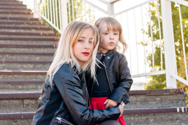 Güzel anne sarışın, kırmızı rujlu ve küçük bir kızı var. Büyük bir portre, kameraya bakıyor, sarılıyor ve gülüyor. Annelik teması ve çocuklu annelerin eğlencesi. Aile görünüşü