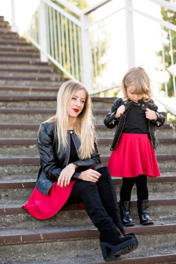 Kırmızı rujlu güzel anne sarışın ve küçük kızı birlikte vakit geçiriyorlar, yürüyorlar, oturuyorlar merdivenlerde koşuyorlar. Kameraya bakıyorlar, sarılıyorlar ve gülüyorlar. Annelik teması ve annelerin eğlencesi.