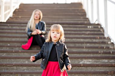 Kırmızı rujlu güzel anne sarışın ve küçük kızı birlikte vakit geçiriyorlar, yürüyorlar, oturuyorlar merdivenlerde koşuyorlar. Kameraya bakıyorlar, sarılıyorlar ve gülüyorlar. Annelik teması ve annelerin eğlencesi.