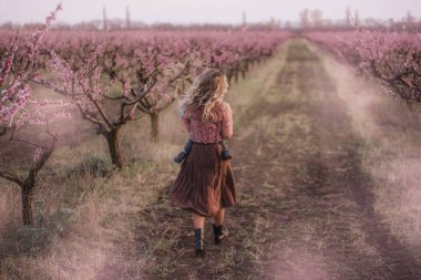 Sarışın, güzel bir anne, kıvırcık saçlı. Gün batımında çiçek açan bahçelerde kucağında küçük bir oğlu var. Çocuk bakımı annelik konsepti. Annesi çocuğu kusuyor, sarılıyor, öpüyor, alnına dokunuyor.